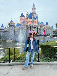 a woman standing in front of a castle with a pink hat and blue jacket on