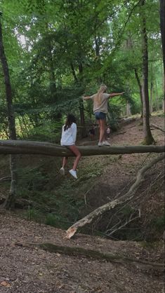 two people jumping over a fallen tree in the woods