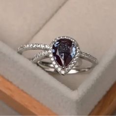 an engagement ring with a pear shaped blue diamond surrounded by white diamonds in a box