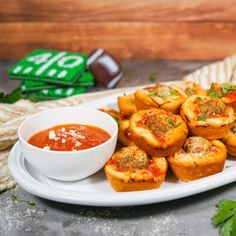 a white plate topped with mini pizzas next to a bowl of tomato sauce and parsley