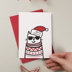 a hand holding up a card with a cat wearing a santa hat and sunglasses on it