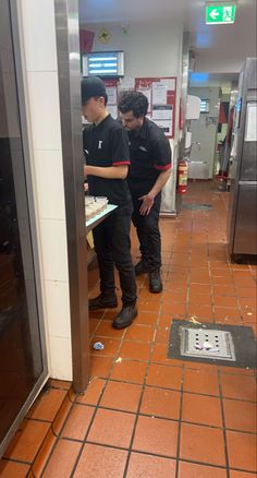 two men standing in front of a pizza oven on a tiled floor next to each other