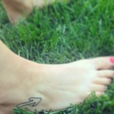 a woman's foot with a tattoo on it sitting in the grass next to a frisbee