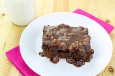 a white plate topped with a piece of chocolate cake next to a glass of milk