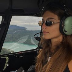 a woman wearing headphones sitting in the cockpit of an airplane looking out into the distance