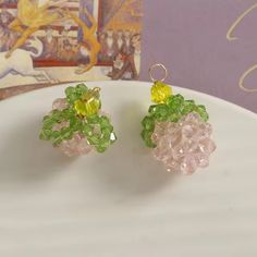 two small green and yellow earrings sitting on top of a white plate next to a painting