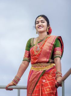 a woman in an orange and green sari standing on a metal rail with her arms crossed