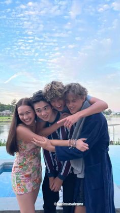 three people hugging each other in front of a swimming pool with the sky and water behind them