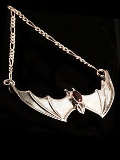 This solid sterling silver Bat pendant would love to hang around your neck. It's wing span is 2 1/4" across. A 16" figaro chain is attached to both wing tips and is included in the price of this piece making the total length of the pendant just over 18". A 5mm x 7mm gemstone is bezel set in the back of the bat. Take flight with one tonight. Please select your desired gemstone in the dropdown options menu. You may choose between a Blue Topaz, Citrine, Amethyst, Peridot, Black Onyx or Mozambique G Gothic Winged Jewelry For Gifts, Gothic Winged Jewelry Gift, Halloween Engraved Sterling Silver Necklaces, Elegant Sterling Silver Halloween Necklace, Collectible Vampire Jewelry For Halloween, Elegant Sterling Silver Necklace For Halloween, Sterling Silver Halloween Pendant Jewelry, Gothic Sterling Silver Jewelry For Halloween, Gothic Gemstone Jewelry For Collectors