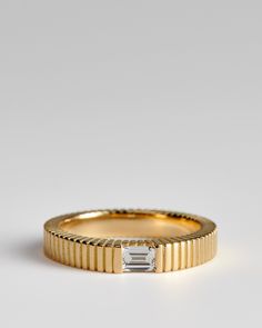 a yellow gold band with a baguette cut diamond in the center, on a white background