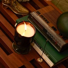 a candle sitting on top of a wooden table next to books and a green lamp