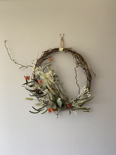 a wreath hanging on the wall with dried flowers and branches around it, in front of a white wall