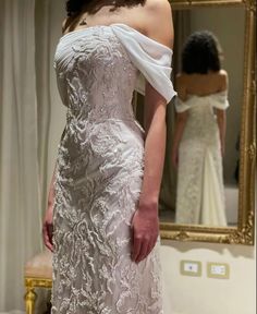 a woman in a wedding dress looking at herself in the mirror with her hand on her hip