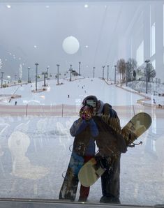 two people standing in front of a window holding snowboards