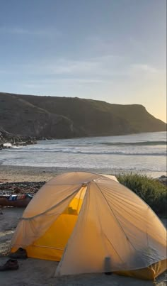 a yellow tent sitting on top of a sandy beach next to the ocean with mountains in the background