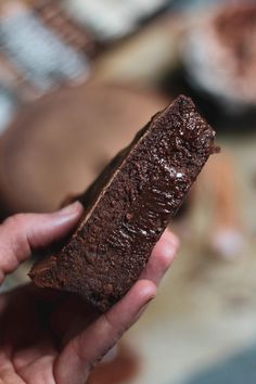 a hand holding a piece of brownie with chocolate frosting on it's side