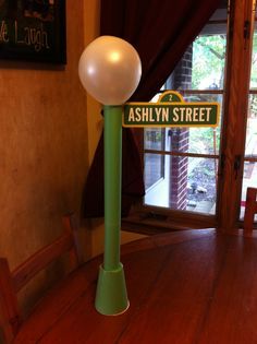 a green pole with a street sign on it's side in front of a window