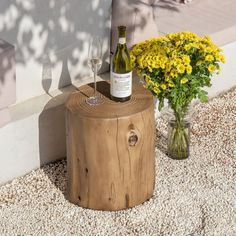 a bottle of wine sitting on top of a wooden stump next to a vase filled with flowers