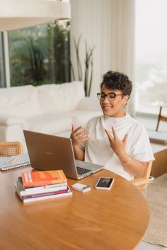 a woman sitting at a table with a laptop computer in front of her and waving