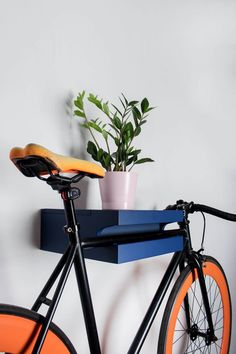 an orange bicycle parked next to a blue shelf with a potted plant on it