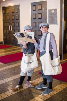 two people standing next to each other holding newspapers