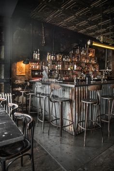 an old bar with several stools and bottles on the wall behind it in a dark room