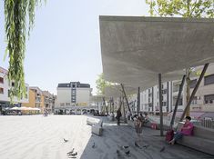 people are sitting on benches in front of some buildings and birds flying around the building