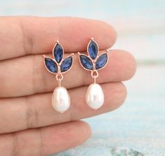 a pair of earrings with blue leaves and pearls on the end of each earring