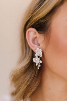 a woman wearing a pair of earrings with flowers on the back of her ear, in front of a white background