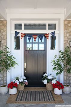 two potted plants sit on the front porch of a house with an american flag banner