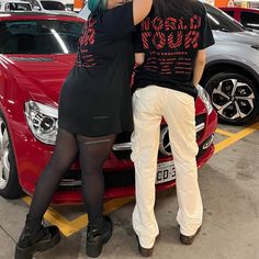 two people standing on the hood of a car in a garage with their arms around each other