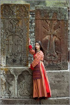 a woman standing next to a stone wall in front of a cross and other carvings