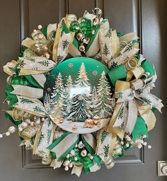 a christmas wreath hanging on the front door decorated with green and gold ribbons, pine trees and snowflakes