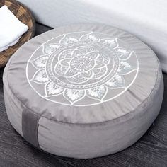 a round ottoman sitting on top of a wooden floor next to a white bed and pillows