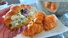 a hand holding a croissant with chicken salad on it next to other pastries