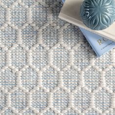 a blue and white rug with two books on top of it next to a vase