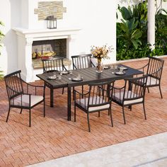 an outdoor dining table with six chairs and a fire place in the back ground area