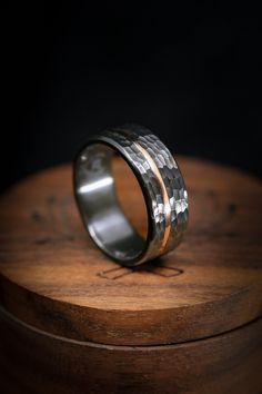 a silver ring with two gold bands on top of a wooden stand in front of a black background