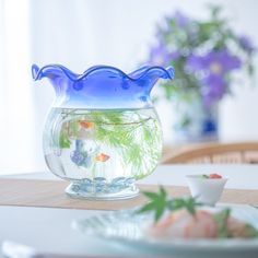 a fish bowl filled with water sitting on top of a table next to a plate