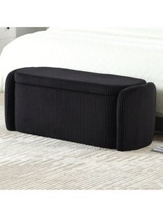 an upholstered black ottoman sits on the floor next to a bed