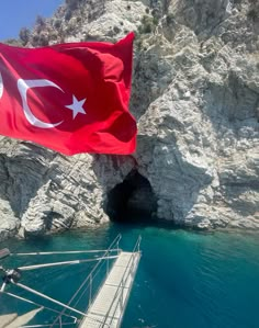 a flag flying in the wind on top of a boat near a rocky cliff face