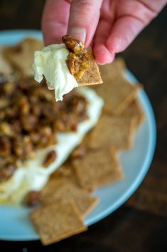 a person holding a cracker over some food on a plate with crackers around it