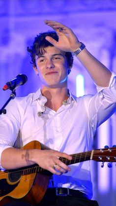 a man holding a guitar while standing in front of a microphone with his hand up