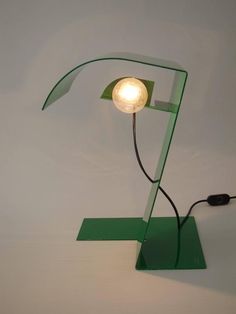 a green table lamp with a white light bulb on it's side and a black cord running through the middle