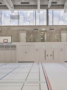 an empty basketball court with several lockers in the center and windows on the far wall