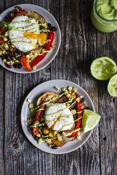 two white plates topped with food next to a glass of green juice and lime wedges