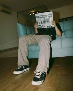 a man sitting on a blue couch reading a book with his feet up in the air