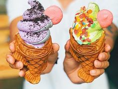 two people holding up ice cream cones with mickey mouse ears on their heads and colorful toppings