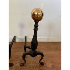 an old fashioned metal ball on a stand with wooden flooring and white wall in the background