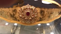 an ornate gold bracelet with red stones and pearls on it's sides, sitting on a glass surface